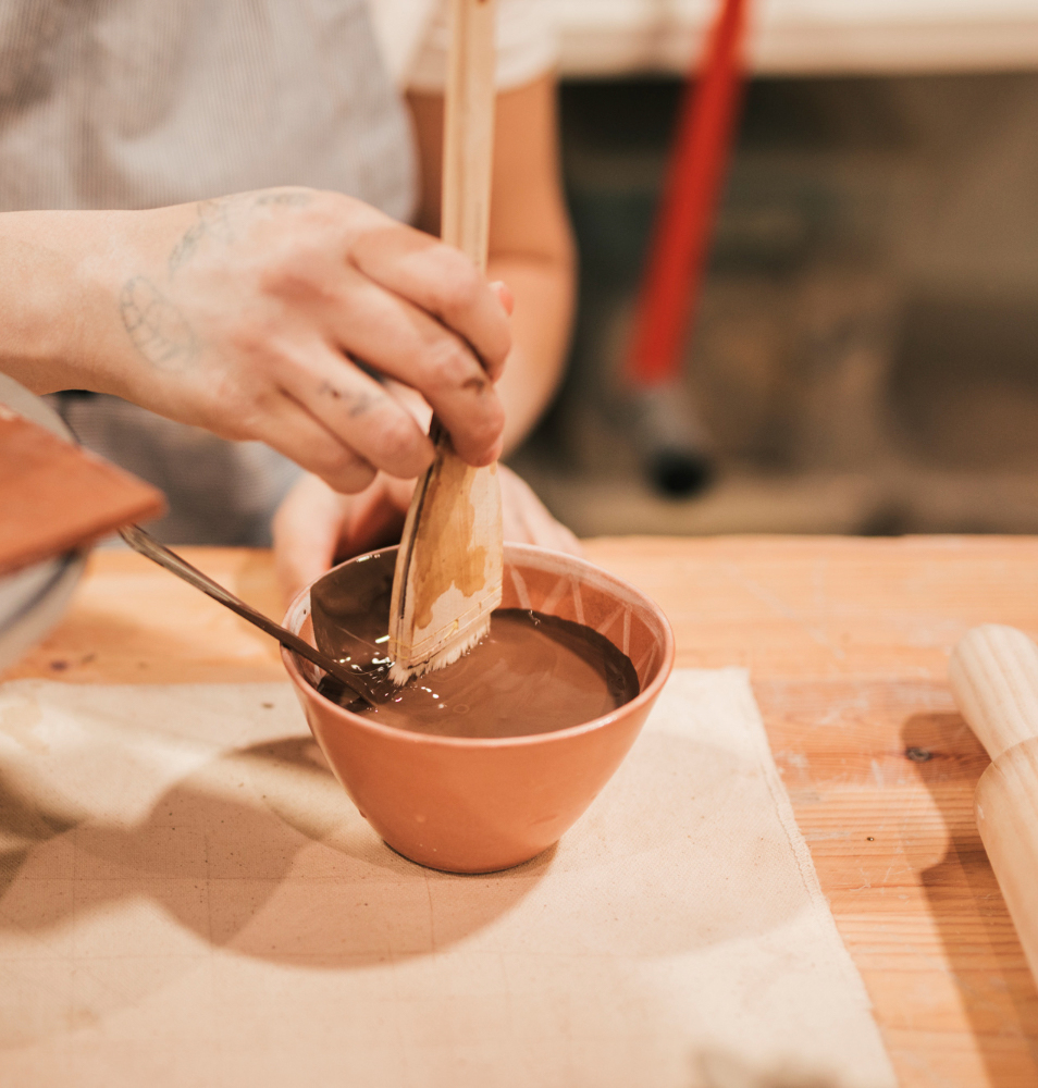 female-potter-s-hand-preparing-the-paint-for-ceramic-bowl-in-the-workshop